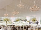 a neutral wedding tent styled with lots of neutral florals and crystal chandeliers is an exquisite space