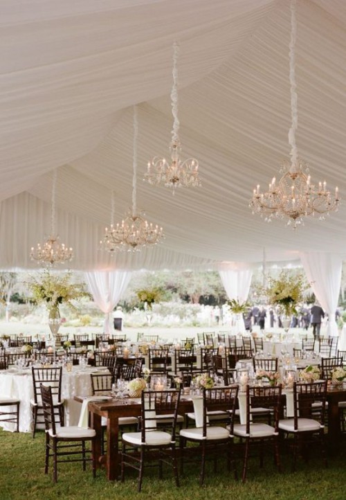a neutral wedding tent styled with lots of neutral florals and crystal chandeliers is an exquisite space