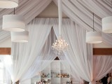 an all-white wedding reception lit up with modern white pendant lamps and a crystal chandelier looks both modern and exquisite