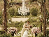 a metal wedding arbor covered with vines and blooms plus a crystal chandelier and greenery and floral arrangement is great for a garden ceremony