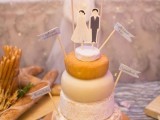 a pretty and cool cheesewheel wedding cake with toppers that mark each tier and funny cardboard couple-shaped toppers plus a banner is a cool idea for every kind of wedding
