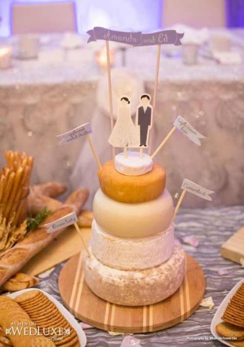 a pretty and cool cheesewheel wedding cake with toppers that mark each tier and funny cardboard couple-shaped toppers plus a banner is a cool idea for every kind of wedding
