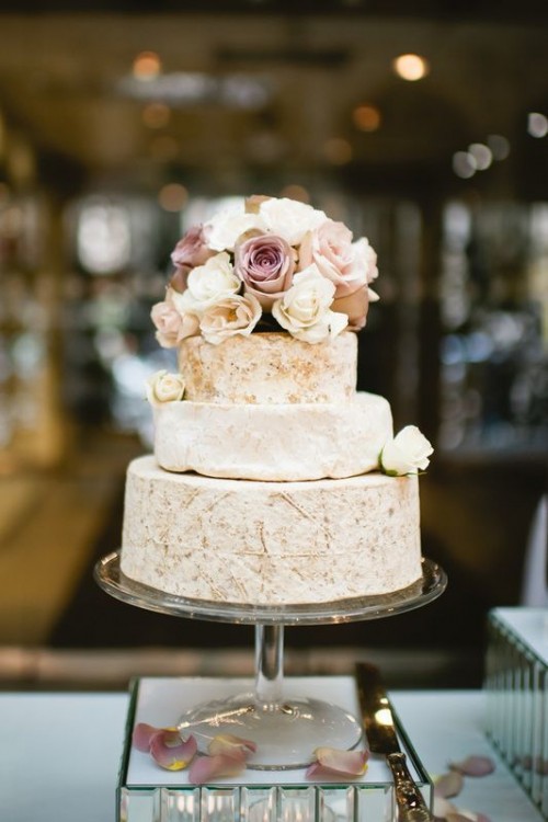 a cheese wheel wedding cake topped with white and pastel blooms is a delicate and chic idea for any kind of wedding