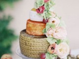 a cheese wheel wedding cake decorated with blush and pink blooms and greenery plus some grapes is a chic idea for a spring or summer wedding