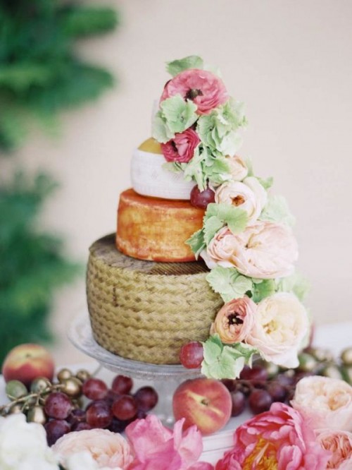 a cheese wheel wedding cake decorated with blush and pink blooms and greenery plus some grapes is a chic idea for a spring or summer wedding