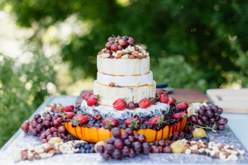 a cheese wheel wedding cake topped with various kinds of fresh berries and fruits is a gorgeous idea for a summer wedding