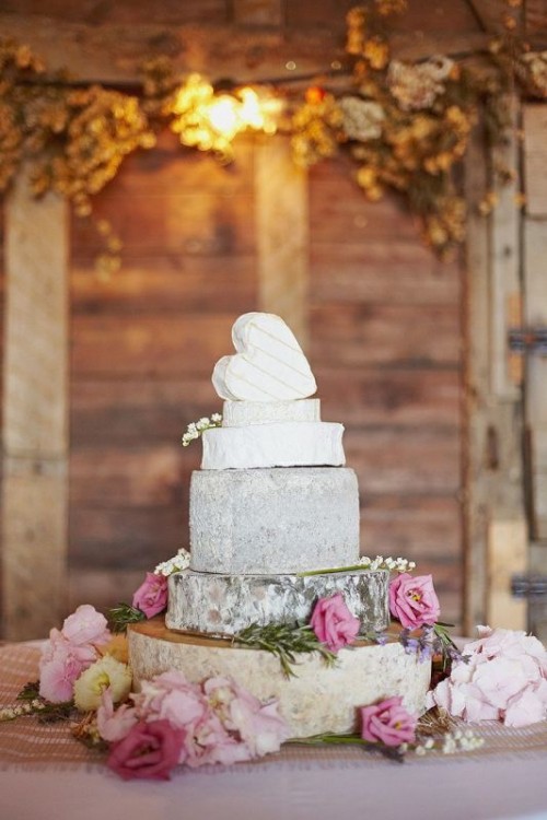 a romantic cheese wheel wedding cake topped with a heart-shaped cheese piece and decorated with pink roses for a rustic wedding