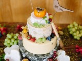 a cheese wheel wedding cake topped with fresh fruit and veggies, with plywood bird toppers with wood burning is a very cool idea