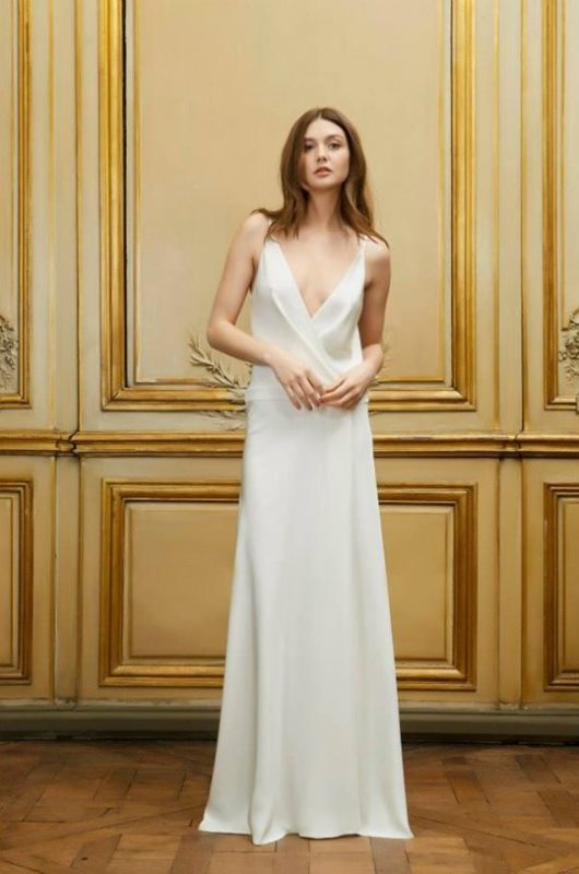 A minimalist plain spaghetti strap wedding dress with a plunging neckline and a draped bodice