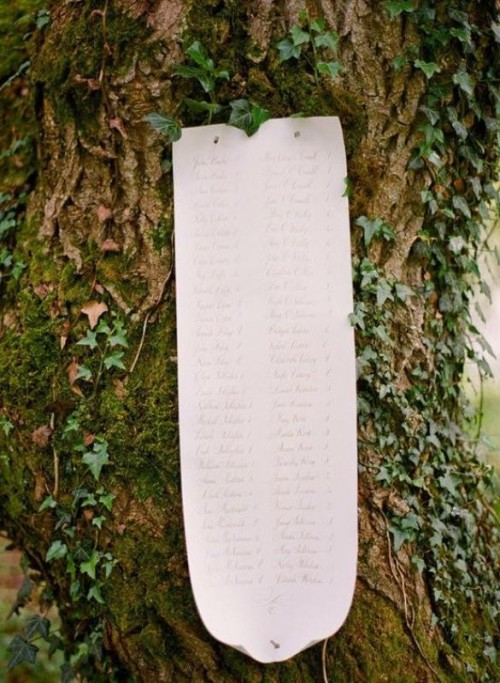 a stylish seating chart of a long paper stripe attached to a tree is a very chic and cool idea for a woodland or fantasy wedding