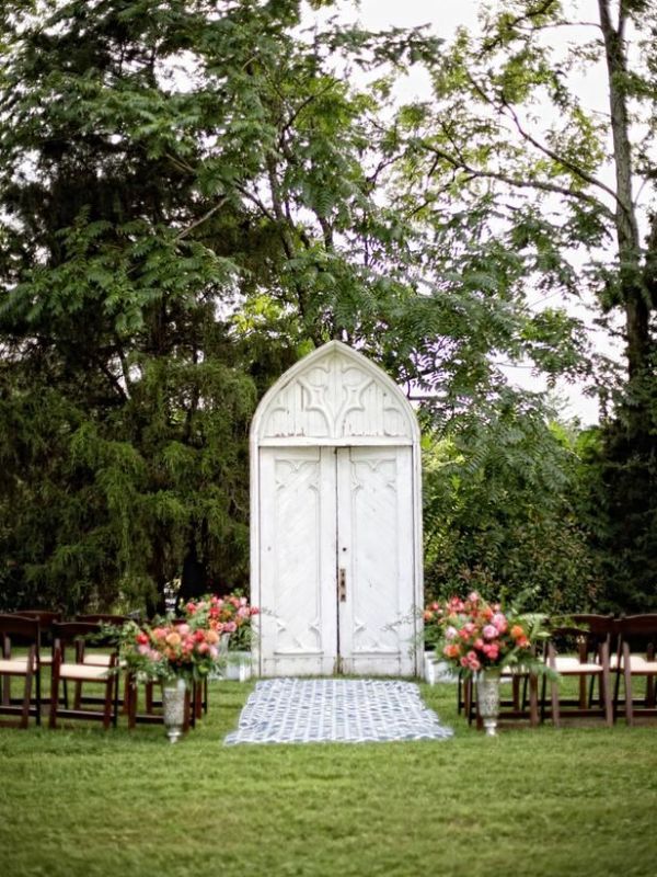 a white vintage double door and bold blooms and greenery lining up the aisle for a vintage infused wedding in the garden