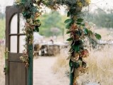 a vintage stained door decorated with foliage and bright leaves plus a copper bucket with greenery and moss are a lovely combo for a fall wedding