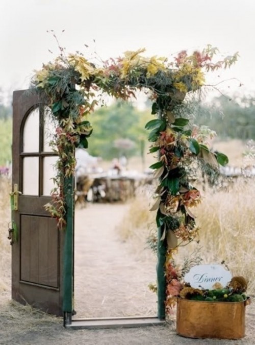 a vintage stained door decorated with foliage and bright leaves plus a copper bucket with greenery and moss are a lovely combo for a fall wedding