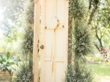 a neutral vintage wedding backdrop of a door decorated with greenery and baby’s breath is a lovely idea for a rustic wedding