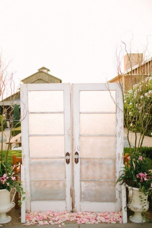 glass double doors with pink petals on the ground and greenery and branches in urns on both sides of the doors