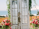 a vintage wedding backdrop of double doors topped with greenery and with neutral urns with pink blooms and greenery