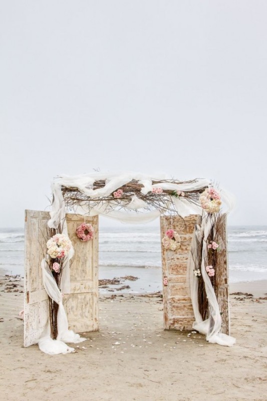 a unique wedding backdrop of vintage doors, a vine wedding arch with tulle and blooms plus a sea view for a vintage beach wedding