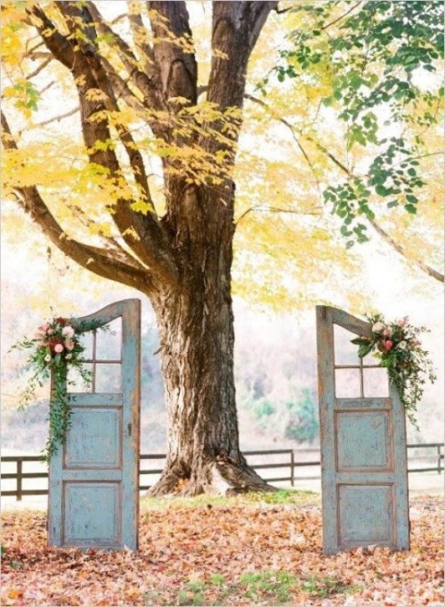a vintage wedding backdrop of a living tree and a couple of shabby chic doors decorated with blooms and greenery