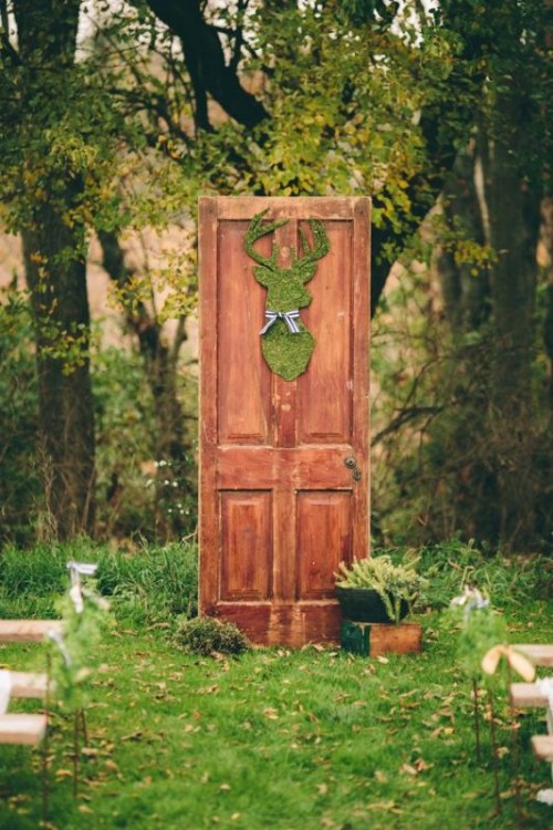 a cool wedding backdrop of a stained door, a moss silhouette and some potted greenery plus a view of the forest