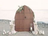 a coastal wedding backdrop of double doors, greenery and white blooms and pillar candles is a creative idea with a vintage feel