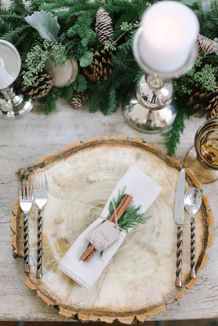 a beautiful winter place setting with an evergreen and pinecone runner, a wood slcie placemats and a cinnamon and evergreen napkin ring