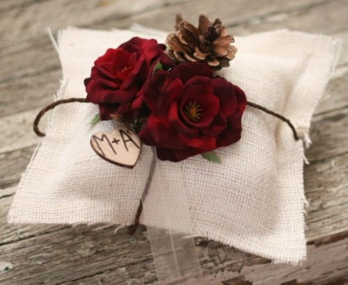 a rustic ring pillow of white burlap, with fabric flowers, pinecones and a wooden heart