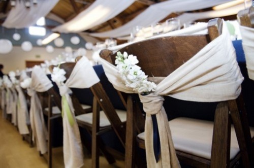 stained wooden chairs with neutral fabric decor and white blooms are great for a rustic wedding