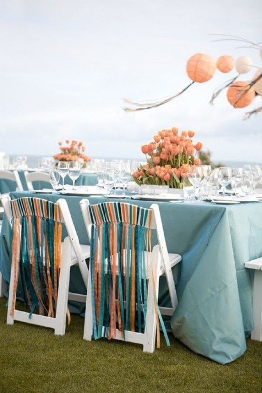 White chairs with turquoise, orange and white fabric ribbons that bring color, interest and eye catchiness to the space and infuse it with brightness