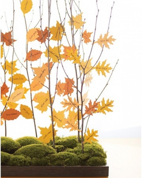a super creative fall wedding seating chart of a moss box with branches and bright paper leaves as escort cards on them