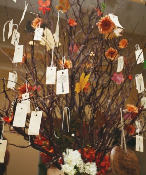 branches with bright leaves and blooms and tags with names hanging from them is a creative wedding seating chart idea