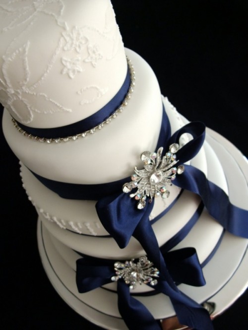 a white patterned wedding cake with navy ribbons and silver embellishments is a very elegant idea