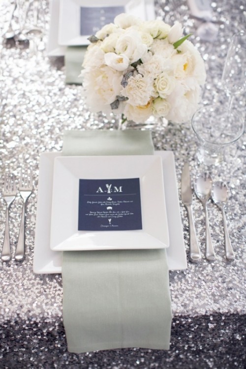a chic tablescape with a silver sequin tablecloth, neutral blooms and a place setting with a navy menu