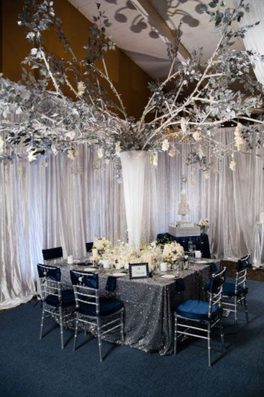 A magical setting with a large sparkling silver centerpiece, navy chairs, a silver sequin tablecloth and lots of white blooms