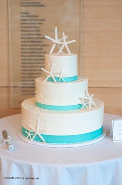 a white wedding cake decorated with bold blue ribbons, with starfish and pearls is a nice idea for a blue beach wedding