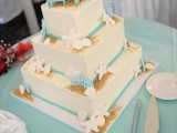 a neutral square cake with bold blue ribbons, seashells, starfish and blue edible chairs on top