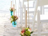 blue jars with neutral and bold blooms, with greenery hanging on ropes for accenting a beach wedding aisle