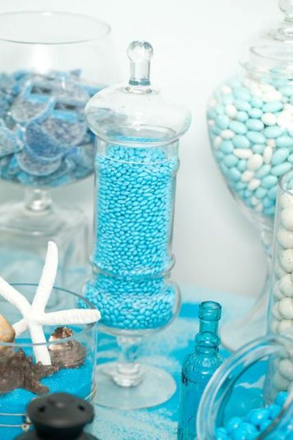 a blue and white beach dessert table with lots of candies and other stuff of all kinds
