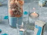 a blue beach wedding tablescape with a light blue tablecloth, blue petals and candles, a blue sand glass with seashells