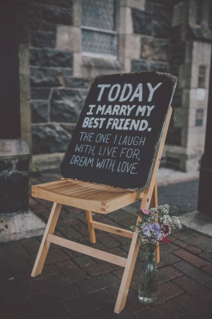 a chalkboard sign placed on a wooden chairs and with blooms at the chair is a lovely idea for a modern space