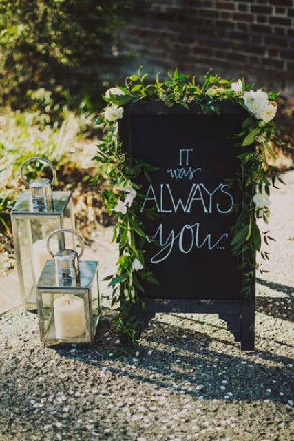 a black chalkboard sign decorated with greenery and with candles around is a lovely decoration for a wedding that you can DIY