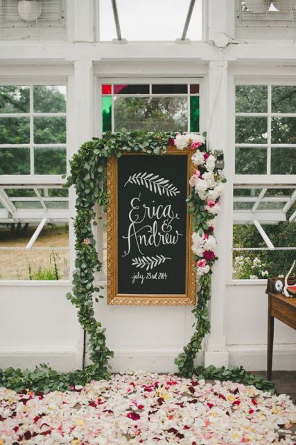 wedding decor with a chalkboard sign and calligraphy, greenery and blooms and lots of petals on the floor is amazing