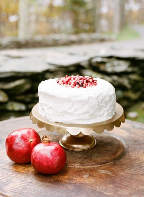 a white buttercream wedding cake topped with pomegranate seeds, with pomegranates around is a lovely idea for a fall or winter wedding