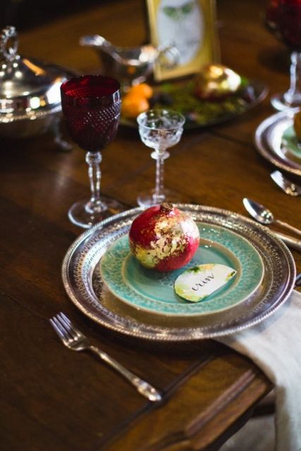 a sophisticated fall wedding tablescape with a gilded charger, a mint-colored plate, a gilded pomegranate and a burgundy glass