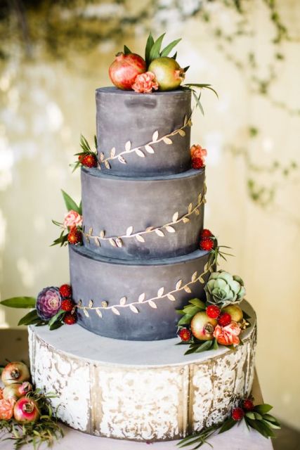 a chalkboard wedding cake topped with pomegranates, apples, greenery, bright blooms and with gilded leaf decor