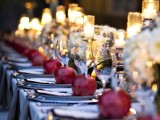 a refined and chic neutral wedding tablescape with a neutral tablecloth and grey napkins, candles in glass candleholders and pomegranates to accent each place setting