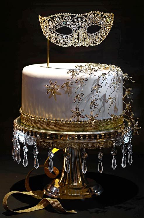 a white wedding cake decorated with shiny gold flowers and a beautiful embellished mask on top is a fantastic idea for a Venice wedding