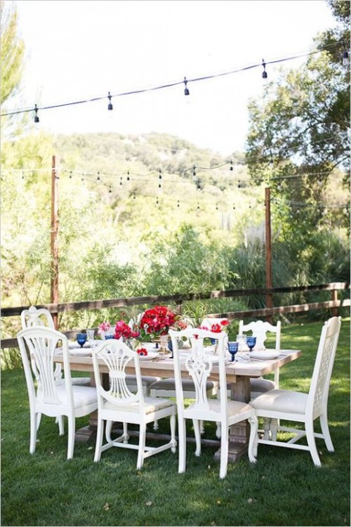 an eclectic backyard wedding reception with a rough wooden table, navy glasses, bold red blooms and elegant vintage white chairs
