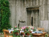 a chic rustic backyard wedding tablescape with an uncovered table, blue and white linens, pink floral centerpieces with greenery and mismatching vintage chairs with wreaths for decor