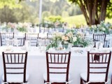an elegant and chic neutral wedding tablescape with white textiles, neutral florals and greenery, candles and chairs with white cushions is a very chic idea