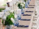 a lovely rustic wedding tablescape with a burlap tablecloth, white and navy napkins, white florals and greenery, candles and candle lanterns
